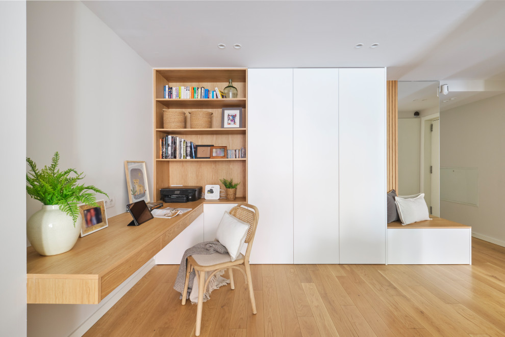Modelo de despacho escandinavo de tamaño medio con paredes blancas, suelo de madera en tonos medios, escritorio empotrado y suelo marrón