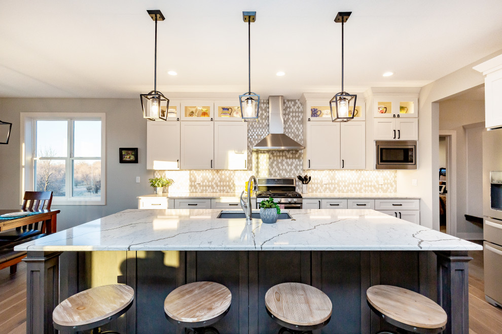 Large transitional l-shaped medium tone wood floor and brown floor open concept kitchen photo with an undermount sink, shaker cabinets, white cabinets, marble countertops, multicolored backsplash, ceramic backsplash, stainless steel appliances, an island and white countertops