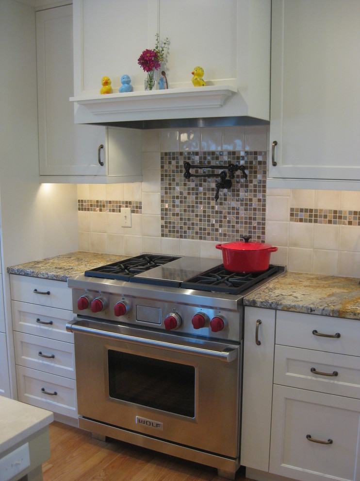 Mid-sized transitional l-shaped light wood floor open concept kitchen photo in Bridgeport with shaker cabinets, white cabinets, granite countertops, white backsplash, porcelain backsplash, stainless steel appliances, an island and an undermount sink