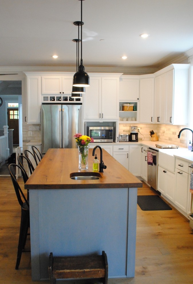 Inspiration for a transitional light wood floor eat-in kitchen remodel in Baltimore with a farmhouse sink, flat-panel cabinets, white cabinets, quartz countertops, white backsplash, stone tile backsplash, stainless steel appliances and an island