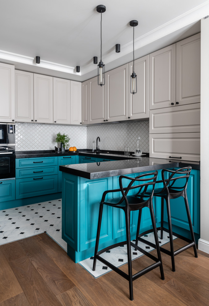 Photo of a contemporary u-shaped kitchen in Moscow with an undermount sink, raised-panel cabinets, blue cabinets, white splashback, mosaic tile splashback, black appliances, a peninsula, white floor and black benchtop.