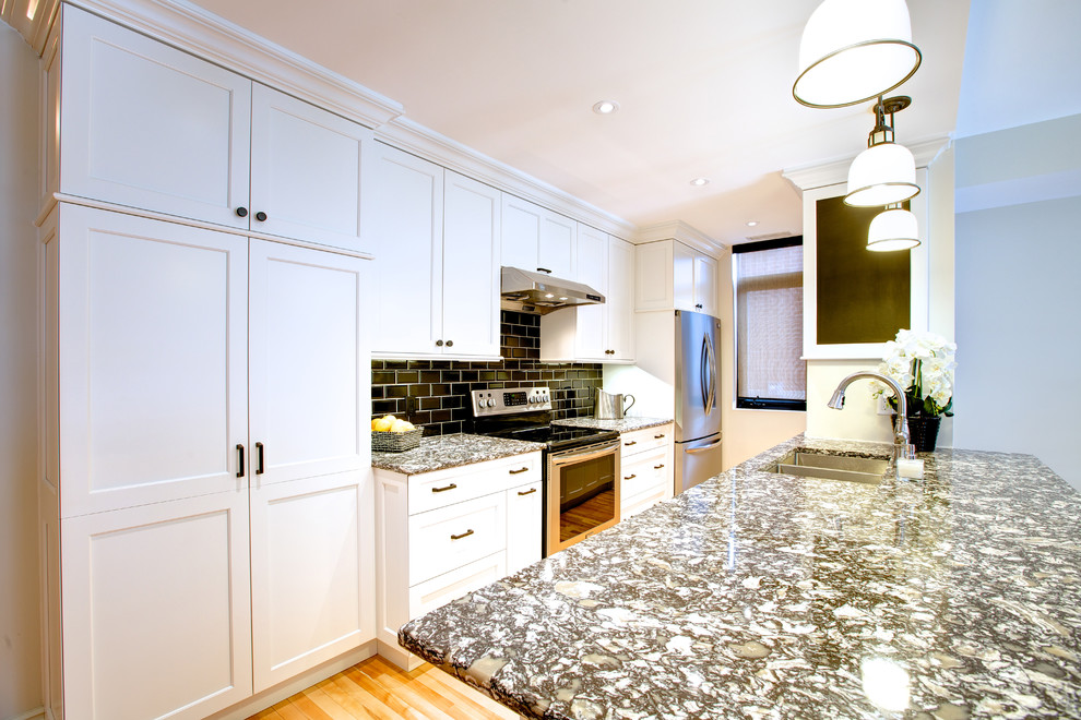 Example of a mid-sized transitional galley light wood floor open concept kitchen design in Ottawa with an undermount sink, shaker cabinets, white cabinets, granite countertops, black backsplash, subway tile backsplash, stainless steel appliances and a peninsula