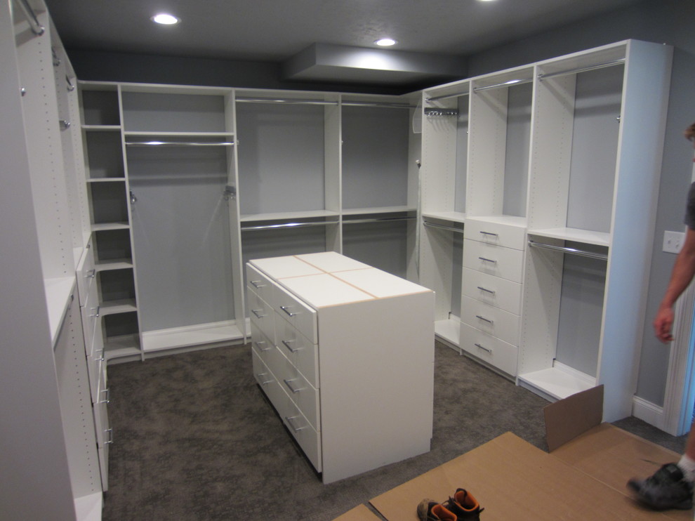 This is an example of a large traditional gender-neutral walk-in wardrobe in Other with flat-panel cabinets, white cabinets and carpet.