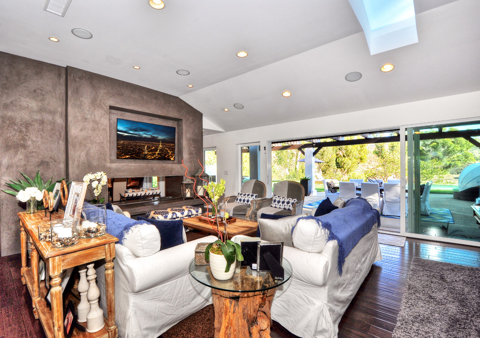 Large transitional formal open concept living room in Orange County with a two-sided fireplace, white walls, dark hardwood floors, a plaster fireplace surround, a wall-mounted tv and brown floor.