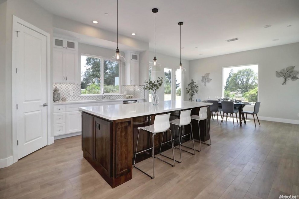 This is an example of a mid-sized contemporary l-shaped eat-in kitchen in Sacramento with an integrated sink, beaded inset cabinets, white cabinets, granite benchtops, white splashback, ceramic splashback, stainless steel appliances, light hardwood floors, with island, beige floor and white benchtop.