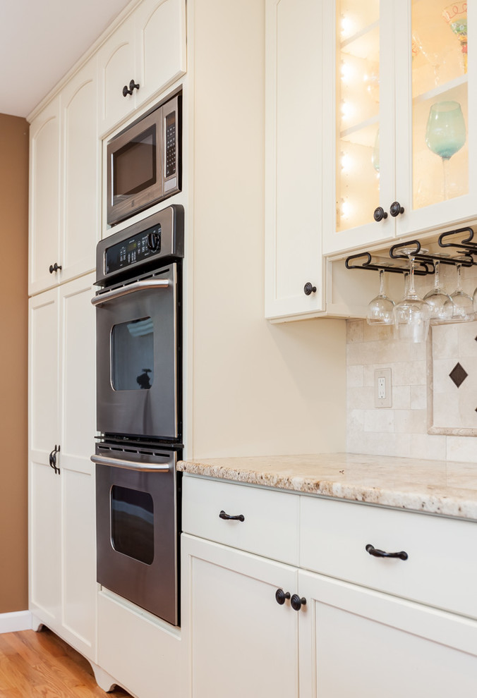 Mid-sized transitional u-shaped light wood floor enclosed kitchen photo in Boston with a double-bowl sink, recessed-panel cabinets, white cabinets, granite countertops, beige backsplash, stone tile backsplash, stainless steel appliances and an island