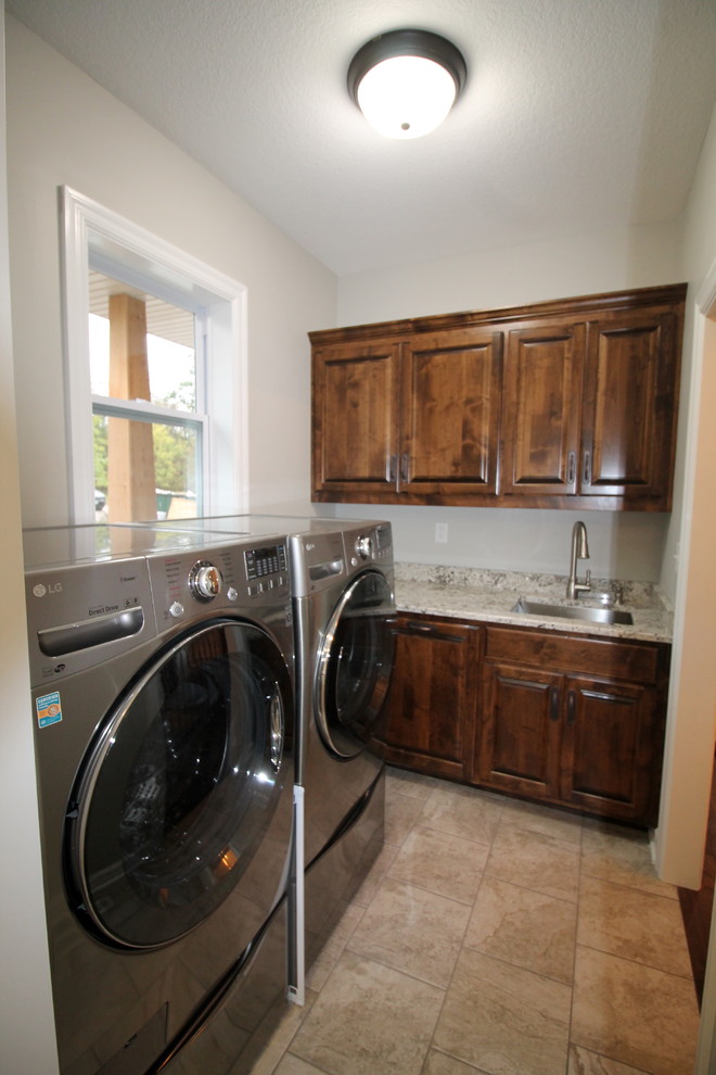 This is an example of a small traditional galley dedicated laundry room in Kansas City with an undermount sink, raised-panel cabinets, brown cabinets, granite benchtops, beige walls, porcelain floors, a side-by-side washer and dryer, beige floor and multi-coloured benchtop.