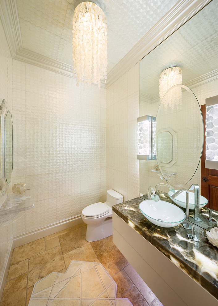 Photo of a mid-sized tropical powder room in Los Angeles with flat-panel cabinets, white cabinets, a one-piece toilet, white tile, glass tile, white walls, travertine floors, a vessel sink, onyx benchtops and beige floor.