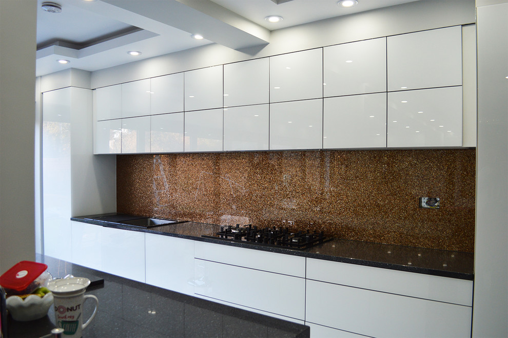 This is an example of a large modern eat-in kitchen in Hertfordshire with flat-panel cabinets, white cabinets, granite benchtops, brown splashback, glass sheet splashback and no island.