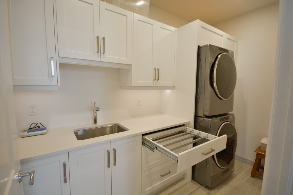 Dedicated laundry room - mid-sized transitional single-wall dedicated laundry room idea in Toronto with an undermount sink, shaker cabinets, white cabinets, quartz countertops, a stacked washer/dryer and white countertops