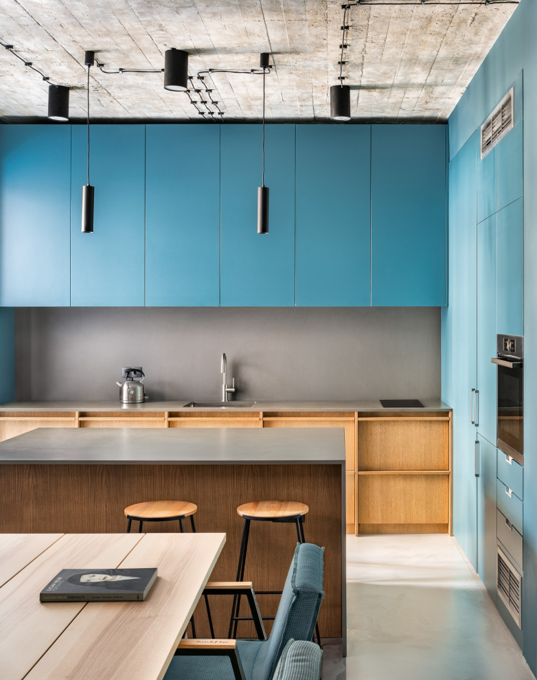 This is an example of a mid-sized industrial kitchen in London with grey splashback, with island, white floor, grey benchtop, an integrated sink, flat-panel cabinets, blue cabinets and stainless steel appliances.
