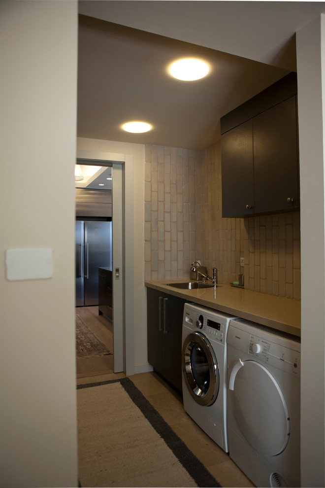 This is an example of a small contemporary single-wall utility room in Other with an undermount sink, flat-panel cabinets, grey cabinets, quartz benchtops, beige walls, limestone floors and a side-by-side washer and dryer.