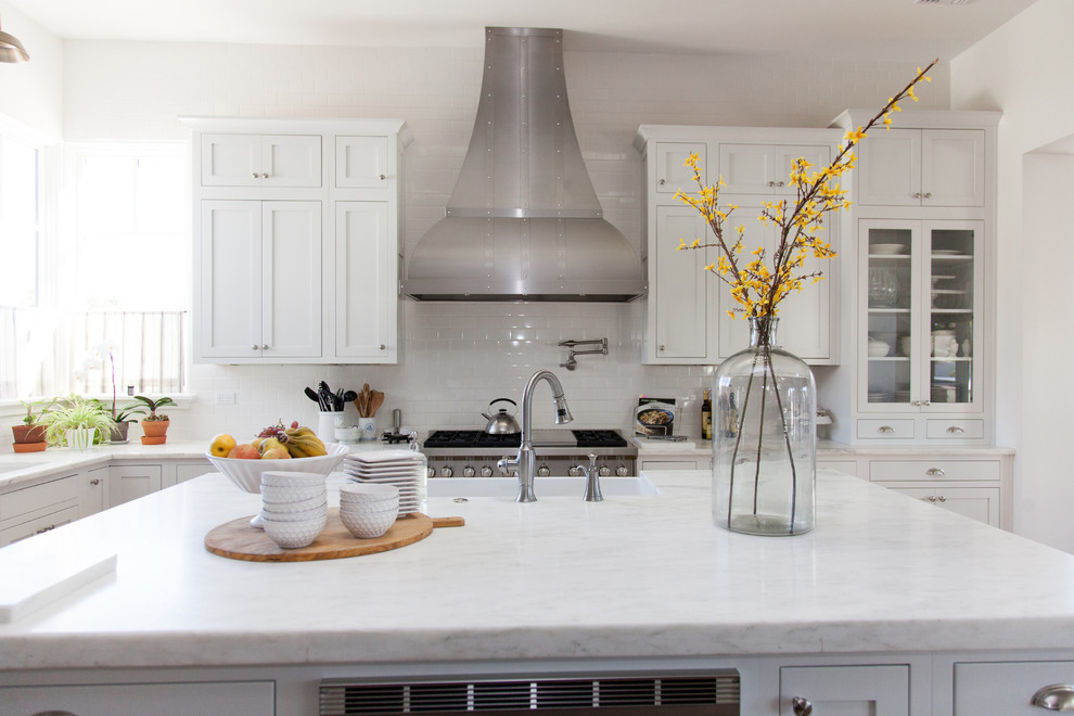 Inspiration for a large transitional l-shaped light wood floor eat-in kitchen remodel in Phoenix with a farmhouse sink, white cabinets, white backsplash, stainless steel appliances, an island, shaker cabinets, stainless steel countertops and porcelain backsplash
