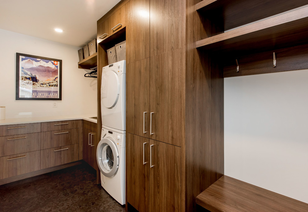 Photo of a mid-sized midcentury l-shaped utility room in Other with a drop-in sink, flat-panel cabinets, medium wood cabinets, quartzite benchtops, white walls, ceramic floors and a stacked washer and dryer.