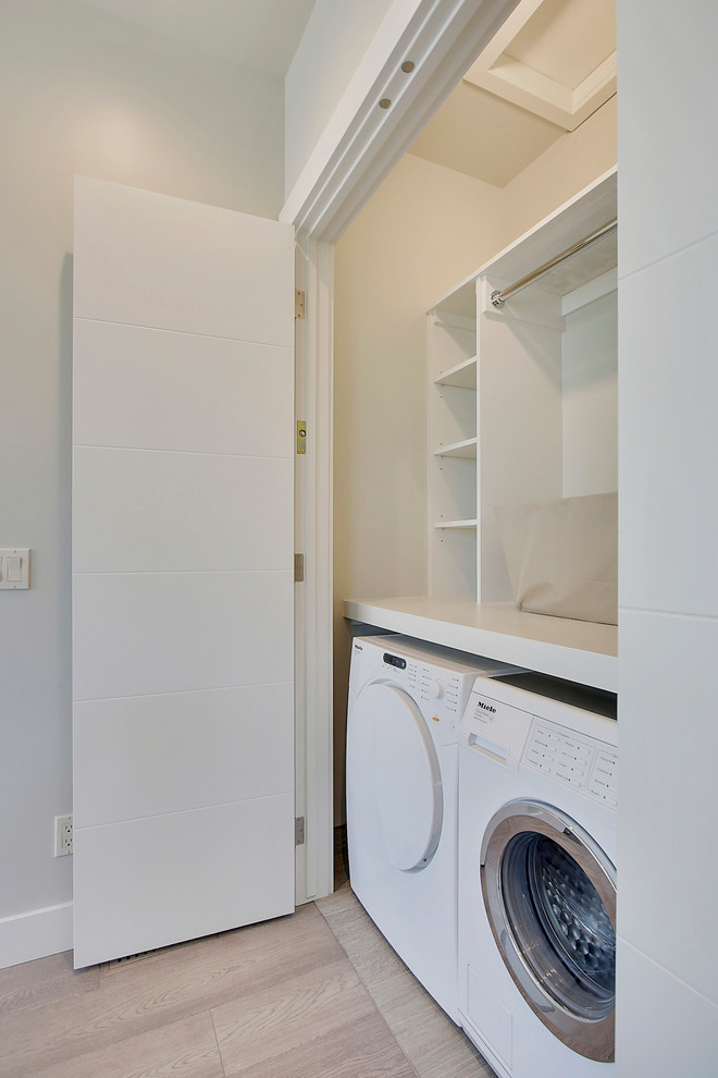 Inspiration for a mid-sized contemporary single-wall laundry cupboard in Calgary with flat-panel cabinets, white cabinets, solid surface benchtops, grey walls, porcelain floors, a side-by-side washer and dryer and grey floor.