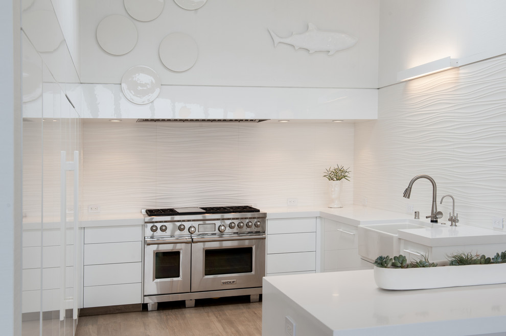 Photo of a contemporary u-shaped open plan kitchen in San Francisco with a farmhouse sink, flat-panel cabinets, white cabinets, quartz benchtops, white splashback, ceramic splashback, white appliances, ceramic floors and with island.
