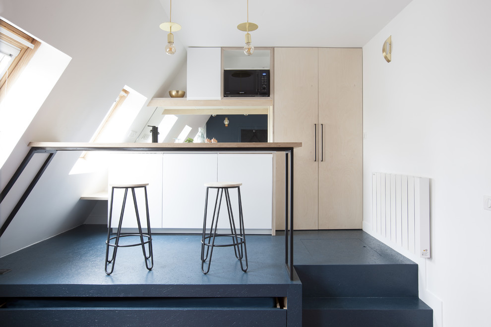 Design ideas for a small contemporary galley open plan kitchen in Paris with flat-panel cabinets, light wood cabinets, black splashback, glass sheet splashback, a peninsula, blue floor, a single-bowl sink, wood benchtops, black appliances and concrete floors.