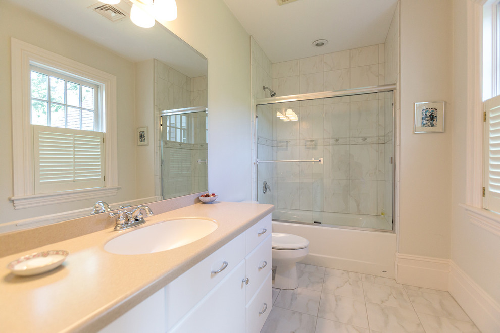 Large traditional 3/4 bathroom in Boston with flat-panel cabinets, white cabinets, an alcove tub, a shower/bathtub combo, a two-piece toilet, beige walls, ceramic floors, a drop-in sink, solid surface benchtops, beige floor, a sliding shower screen and beige benchtops.