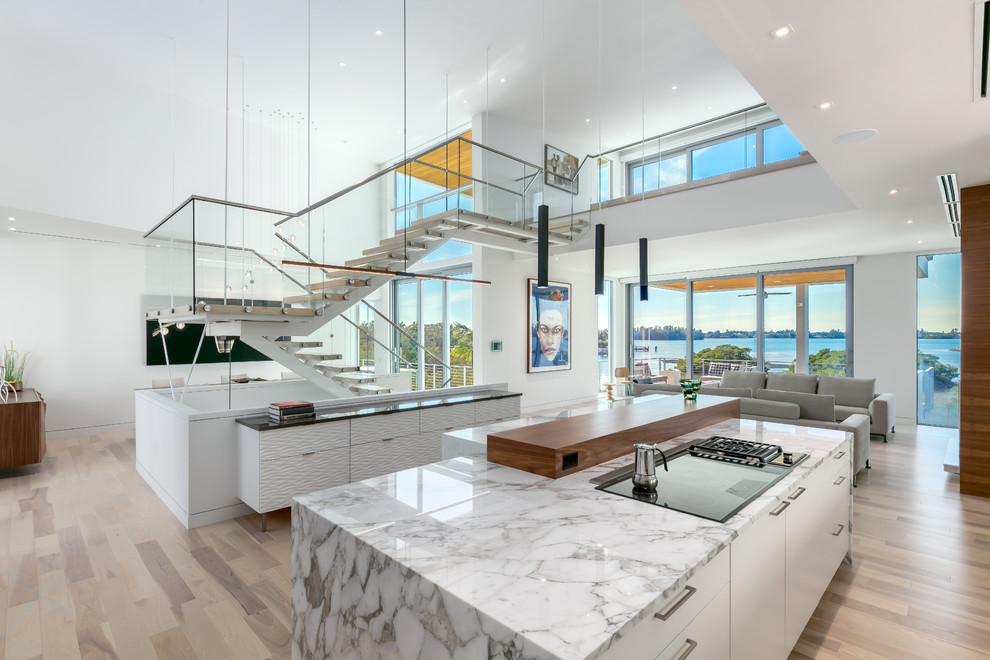 Design ideas for a large contemporary l-shaped open plan kitchen in Tampa with a triple-bowl sink, flat-panel cabinets, white cabinets, quartzite benchtops, white splashback, window splashback, panelled appliances, light hardwood floors, with island and multi-coloured floor.