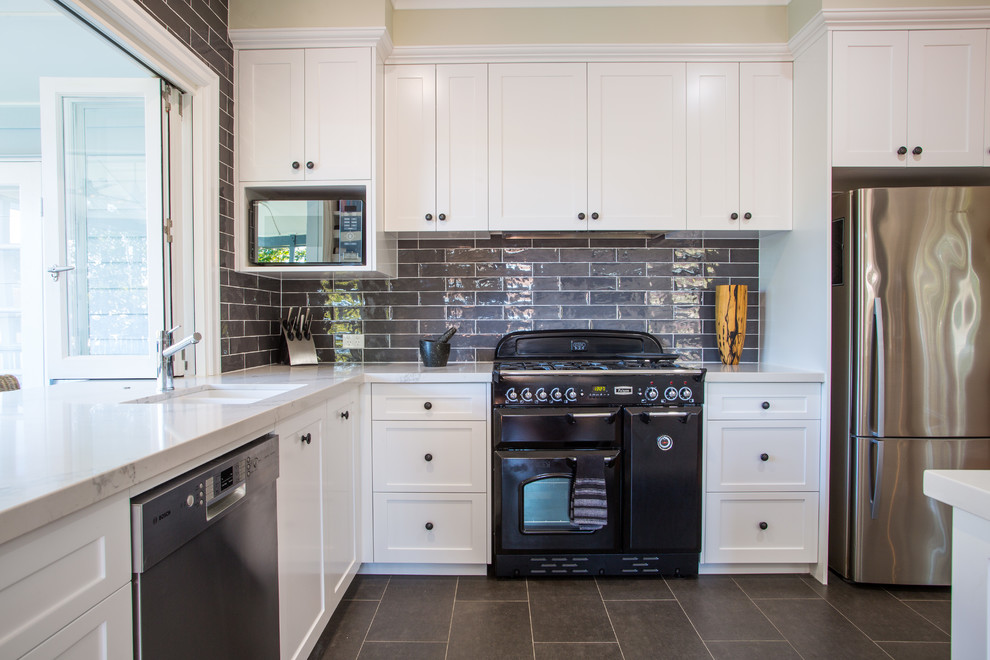 This is an example of a large traditional l-shaped open plan kitchen in Brisbane with an undermount sink, shaker cabinets, white cabinets, quartz benchtops, grey splashback, subway tile splashback, black appliances, ceramic floors, with island and grey floor.