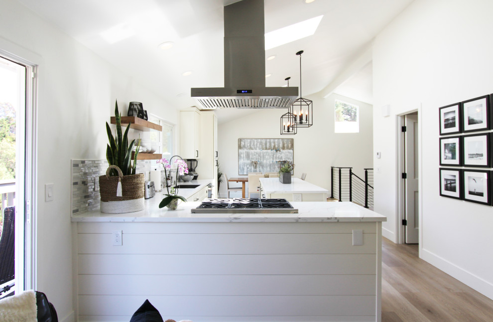 Eat-in kitchen - mid-sized transitional l-shaped vinyl floor, brown floor and vaulted ceiling eat-in kitchen idea with an undermount sink, shaker cabinets, white cabinets, quartz countertops, multicolored backsplash, mosaic tile backsplash, stainless steel appliances, an island and white countertops