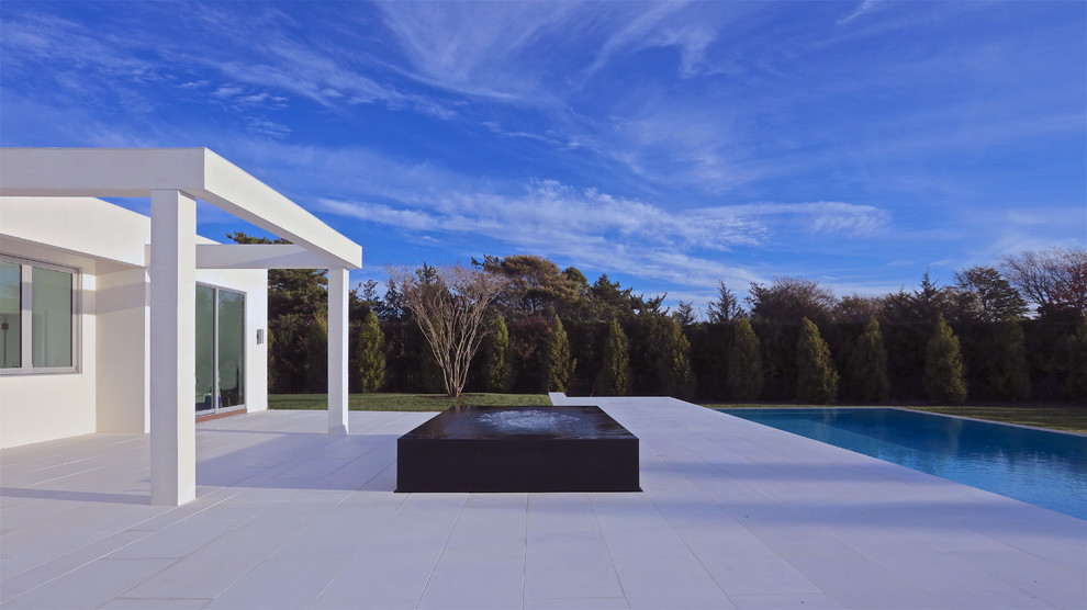 Modern backyard rectangular infinity pool in New York with concrete pavers and a pool house.