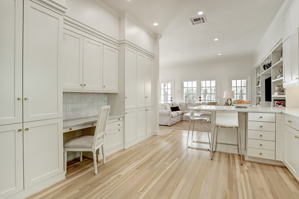 Mid-sized traditional galley separate kitchen in Houston with a drop-in sink, recessed-panel cabinets, white cabinets, quartz benchtops, white splashback, ceramic splashback, stainless steel appliances, light hardwood floors, no island, white floor and white benchtop.