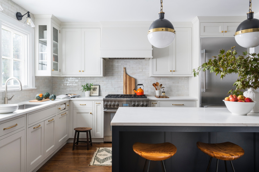 Photo of a small traditional u-shaped kitchen/diner in New York with a triple-bowl sink, shaker cabinets, blue cabinets, marble worktops, white splashback, ceramic splashback, stainless steel appliances, dark hardwood flooring, an island, brown floors and white worktops.