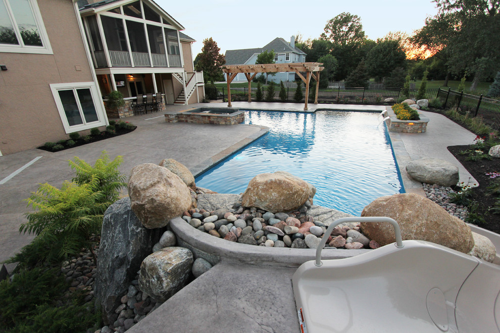 Photo of a large contemporary backyard l-shaped natural pool in Kansas City with a hot tub and stamped concrete.