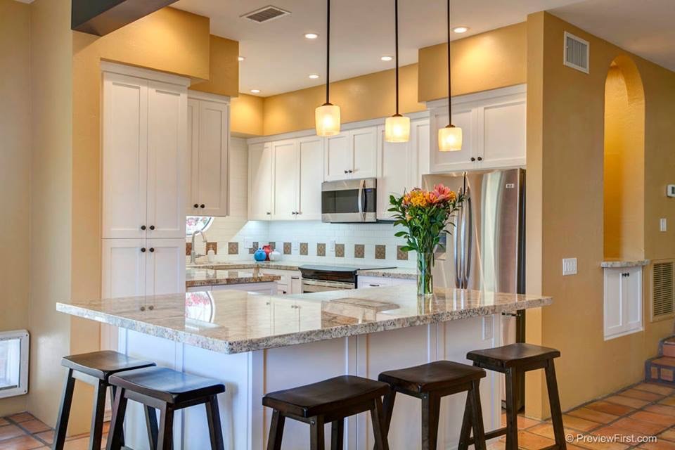 This is an example of a mid-sized mediterranean u-shaped open plan kitchen in San Diego with an undermount sink, shaker cabinets, white cabinets, granite benchtops, white splashback, glass tile splashback, stainless steel appliances, terra-cotta floors and with island.
