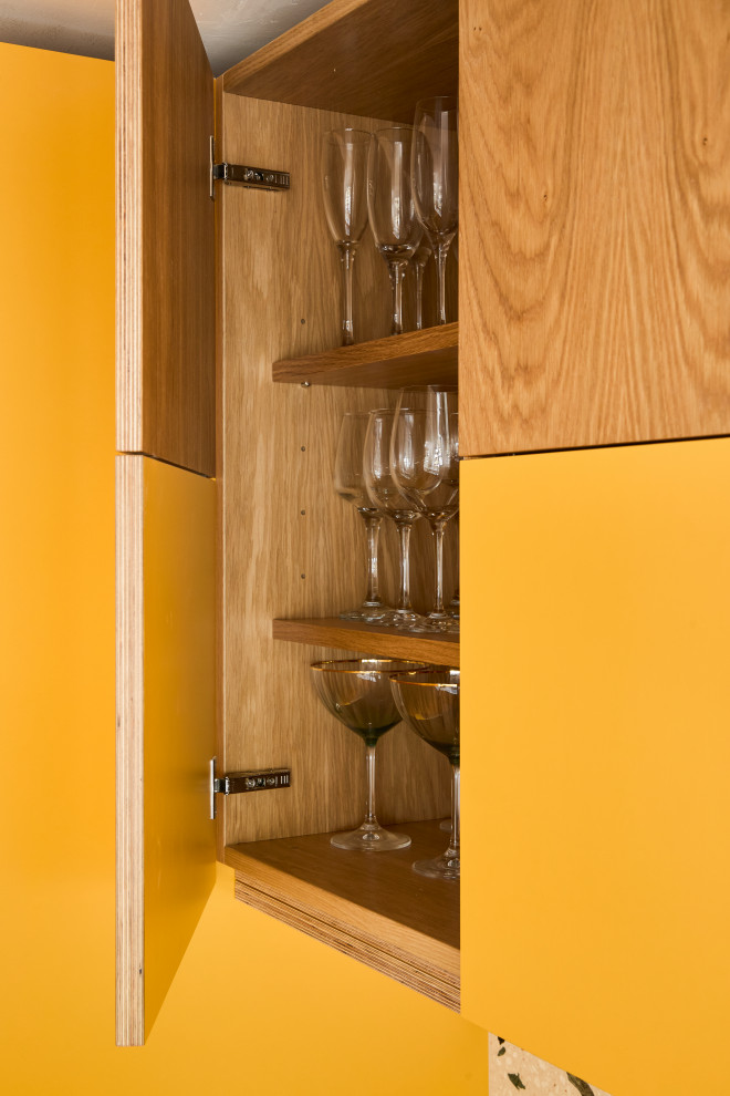Große Mid-Century Wohnküche in L-Form mit Unterbauwaschbecken, flächenbündigen Schrankfronten, gelben Schränken, Arbeitsplatte aus Terrazzo, bunter Rückwand, Rückwand aus Stein, Küchengeräten aus Edelstahl, braunem Holzboden, Kücheninsel, braunem Boden und bunter Arbeitsplatte in Kent