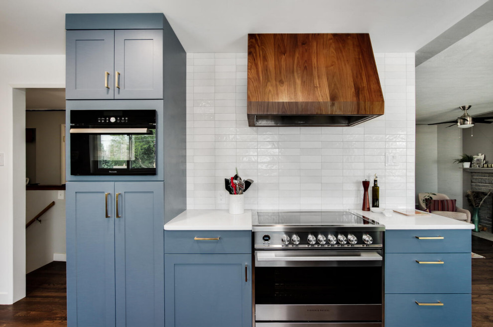Inspiration for a mid-sized transitional l-shaped dark wood floor and brown floor eat-in kitchen remodel in Denver with a single-bowl sink, shaker cabinets, blue cabinets, quartz countertops, white backsplash, porcelain backsplash, stainless steel appliances, a peninsula and white countertops