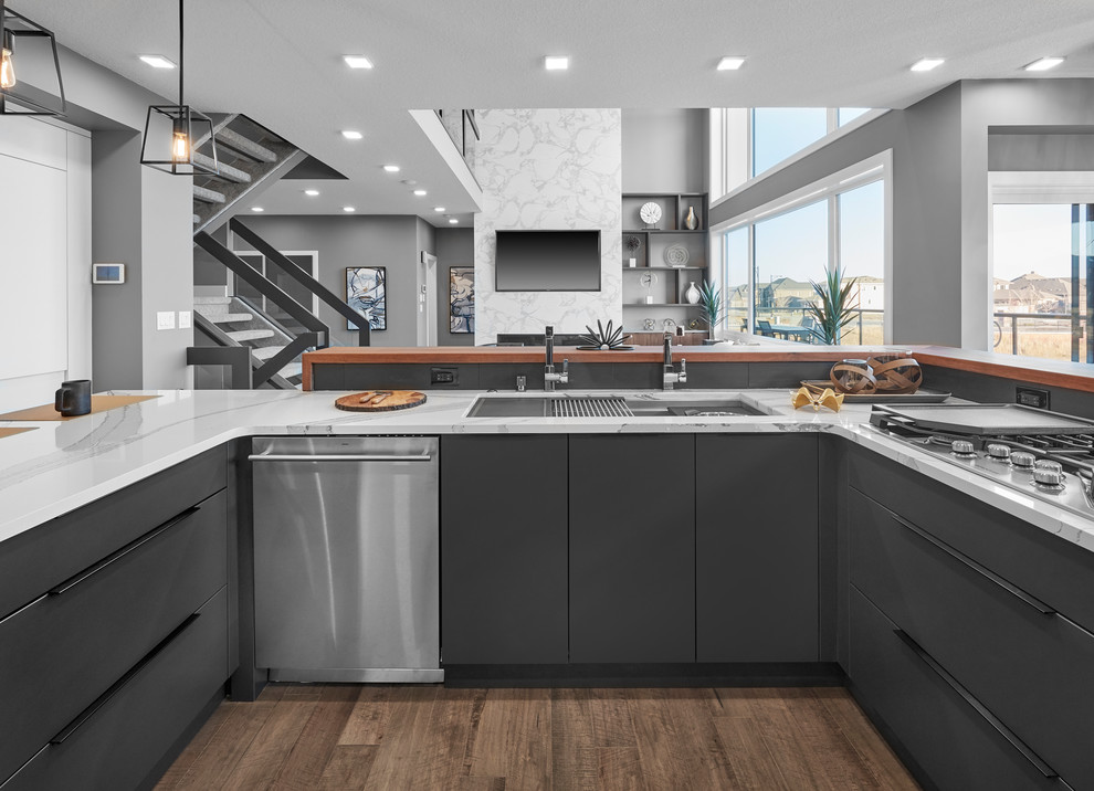 Photo of a large modern l-shaped eat-in kitchen in Edmonton with a triple-bowl sink, flat-panel cabinets, grey cabinets, quartz benchtops, grey splashback, porcelain splashback, stainless steel appliances, medium hardwood floors, with island, brown floor and white benchtop.