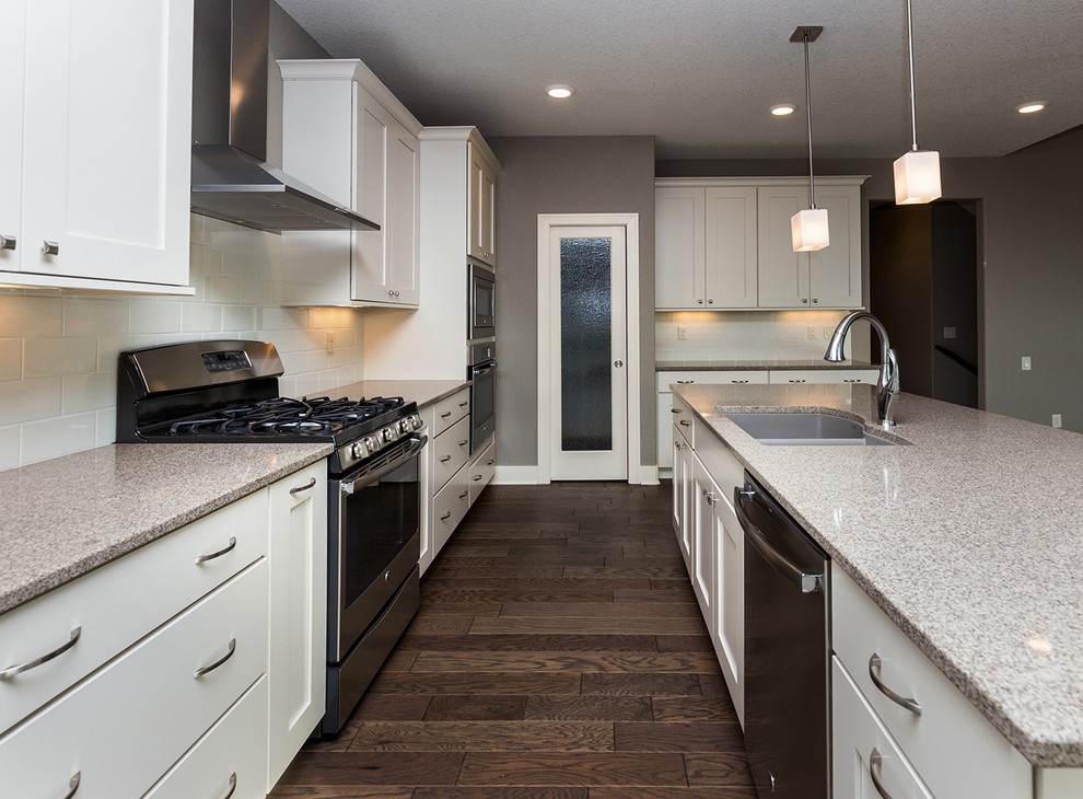 Open concept kitchen - transitional l-shaped dark wood floor open concept kitchen idea with an undermount sink, shaker cabinets, white cabinets, quartz countertops, white backsplash, subway tile backsplash, stainless steel appliances and an island