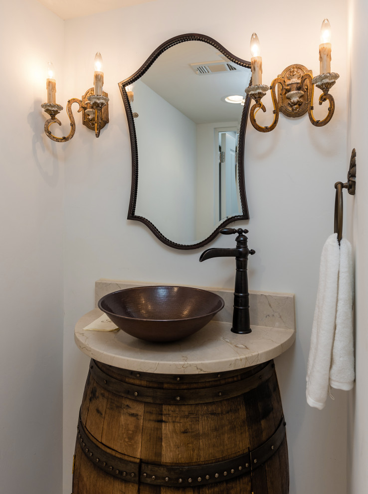Inspiration for a mid-sized mediterranean powder room in Dallas with brown cabinets, white walls, travertine floors, a vessel sink, marble benchtops, beige floor, beige benchtops and a freestanding vanity.