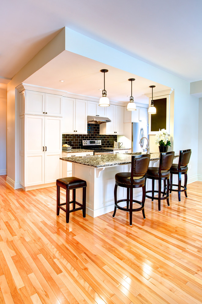 Mid-sized transitional galley light wood floor open concept kitchen photo in Ottawa with an undermount sink, shaker cabinets, white cabinets, granite countertops, black backsplash, subway tile backsplash, stainless steel appliances and a peninsula