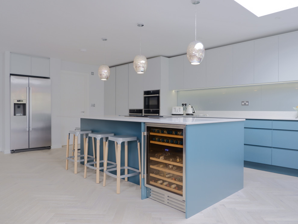 This is an example of a large contemporary l-shaped open plan kitchen in London with a built-in sink, flat-panel cabinets, green cabinets, quartz worktops, grey splashback, glass sheet splashback, stainless steel appliances, light hardwood flooring, an island, brown floors and white worktops.