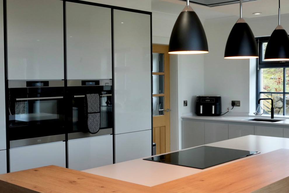 Large modern grey and black open plan kitchen with black appliances, an island and white worktops.