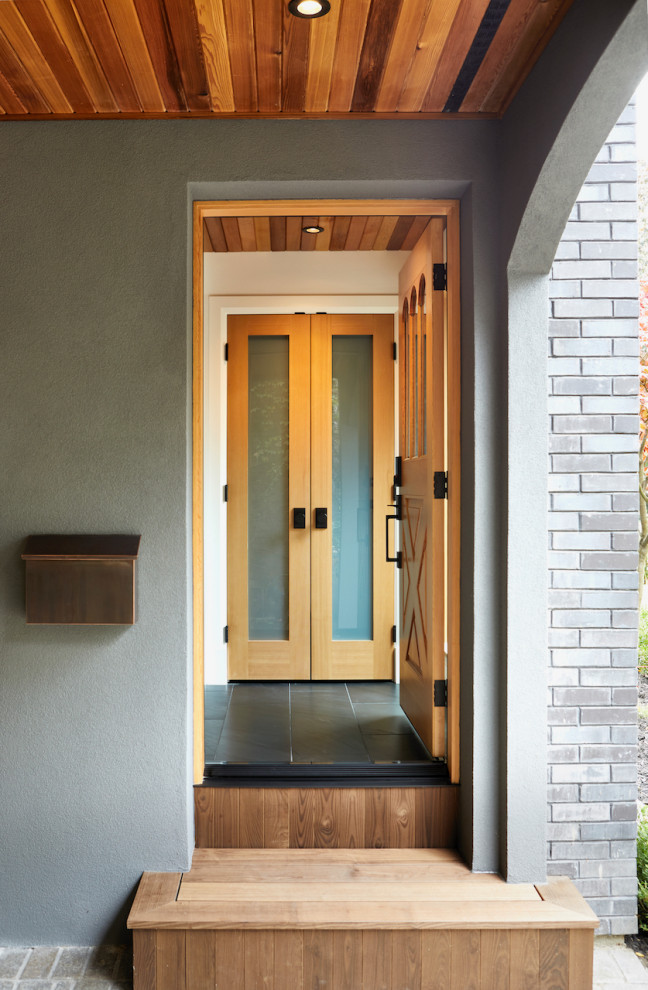 Cette image montre une grande entrée avec un vestiaire, un mur blanc, une porte en bois clair, un sol noir, un plafond en bois et une porte simple.