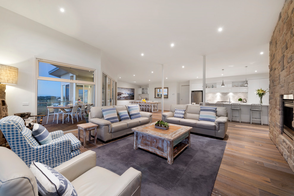 This is an example of a beach style living room in Melbourne with white walls, light hardwood floors, a standard fireplace, a stone fireplace surround and no tv.
