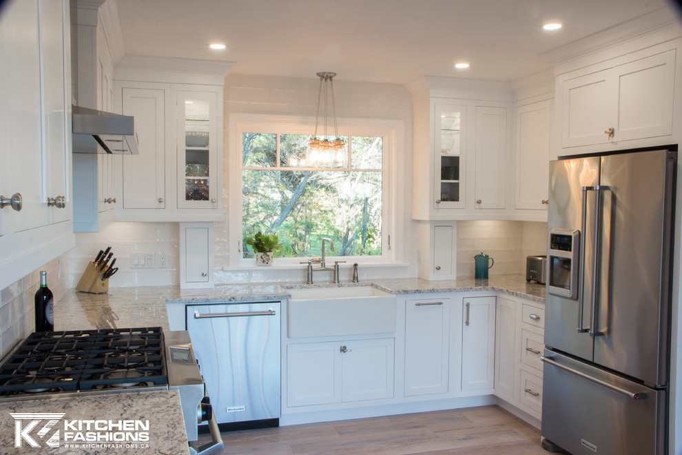 Large transitional u-shaped light wood floor eat-in kitchen photo with a farmhouse sink, shaker cabinets, white cabinets, granite countertops, white backsplash, subway tile backsplash, stainless steel appliances and no island