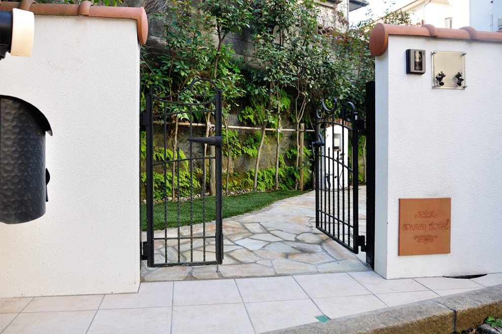 This is an example of a medium sized mediterranean front garden in Yokohama with a gate, natural stone paving and a metal fence.