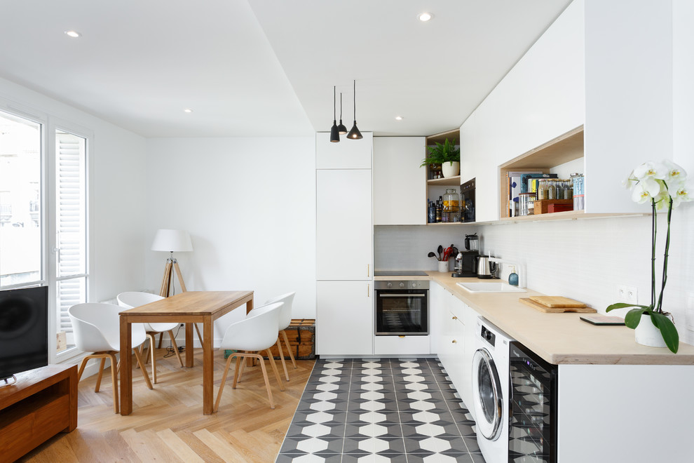 Design ideas for a mid-sized scandinavian l-shaped open plan kitchen in Paris with a single-bowl sink, flat-panel cabinets, white cabinets, wood benchtops, white splashback, ceramic splashback, stainless steel appliances, cement tiles, grey floor, beige benchtop and no island.