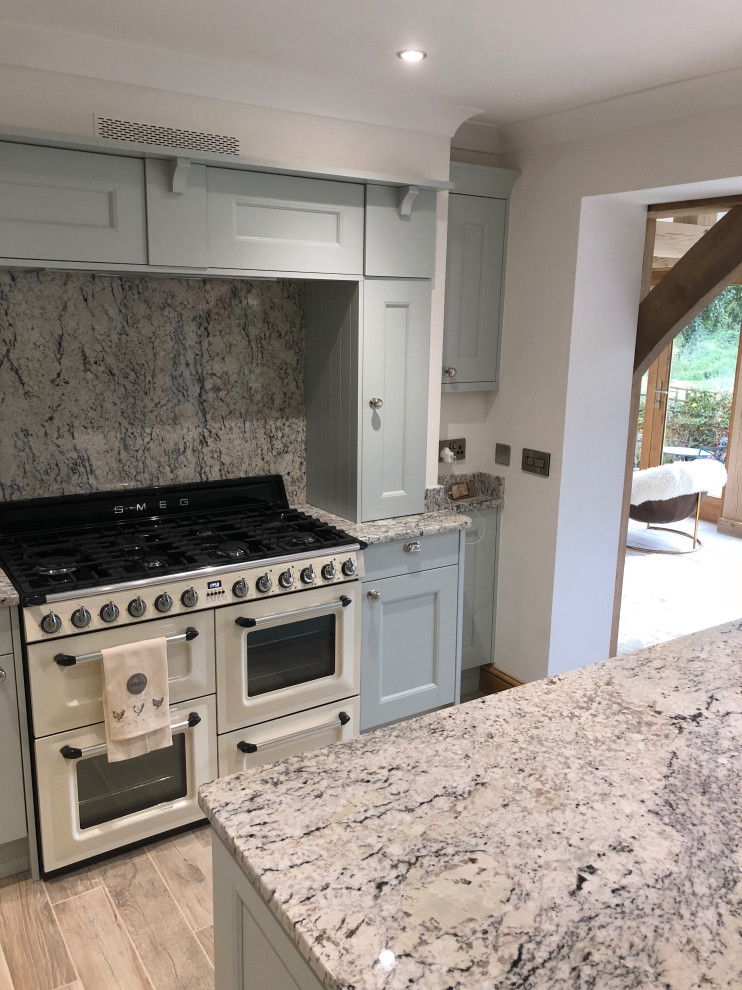 This is an example of a large rural kitchen in Other with a belfast sink, shaker cabinets, blue cabinets, granite worktops, grey splashback, granite splashback, porcelain flooring, an island and grey worktops.
