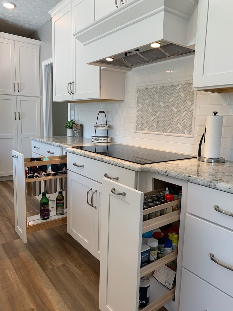 This is an example of a mid-sized transitional l-shaped open plan kitchen in Other with an undermount sink, shaker cabinets, white cabinets, granite benchtops, white splashback, subway tile splashback, stainless steel appliances, vinyl floors, with island, brown floor and white benchtop.