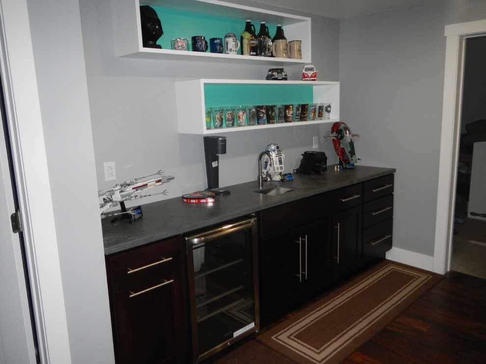 This is an example of a small contemporary single-wall wet bar in Other with an undermount sink, recessed-panel cabinets, dark wood cabinets, solid surface benchtops and vinyl floors.