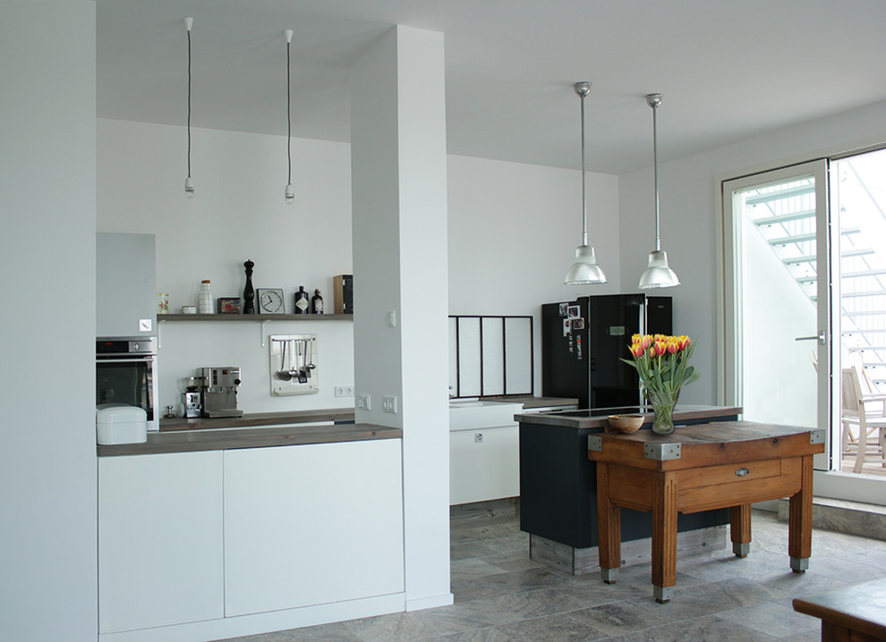 Inspiration for a large industrial galley open plan kitchen in Berlin with a drop-in sink, flat-panel cabinets, white cabinets, wood benchtops, white splashback, glass sheet splashback, stainless steel appliances, cement tiles, with island and grey floor.