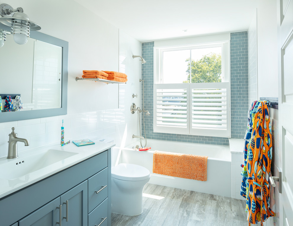Mid-sized beach style kids bathroom in Other with shaker cabinets, blue cabinets, blue tile, subway tile, white walls, an integrated sink, white benchtops, an alcove tub, an open shower, a one-piece toilet, porcelain floors, solid surface benchtops and grey floor.