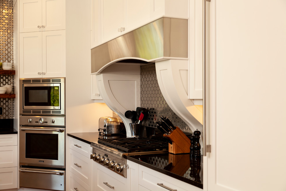 Example of a mid-sized transitional l-shaped enclosed kitchen design with shaker cabinets, white cabinets, stainless steel appliances, an island and black countertops