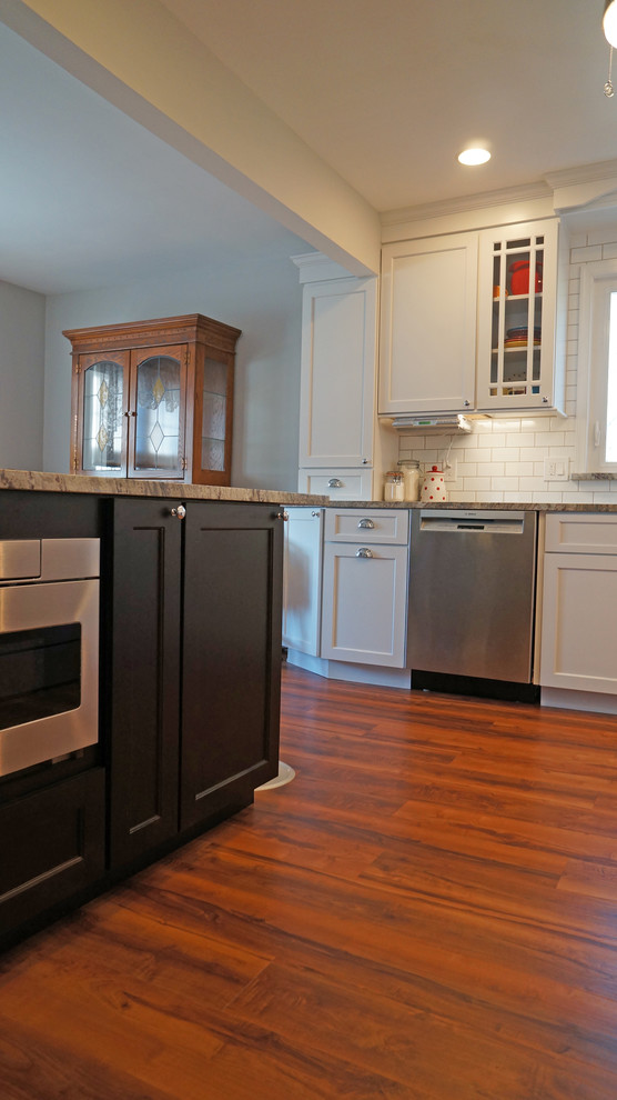 Photo of a mid-sized transitional l-shaped eat-in kitchen in Philadelphia with an undermount sink, shaker cabinets, white cabinets, granite benchtops, white splashback, subway tile splashback, stainless steel appliances, vinyl floors, a peninsula, brown floor and grey benchtop.